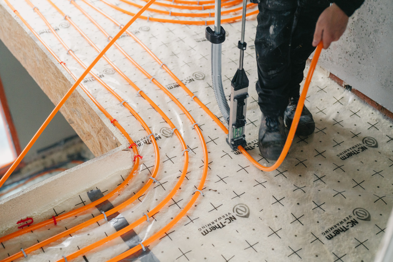 Installatie van energiezuinige vloerverwarming door NC Therm Technieker plaatst oranje verwarmingsbuizen op isolerende onderlaag tijdens de installatie van een energiezuinig vloerverwarmingssysteem van NC Therm.