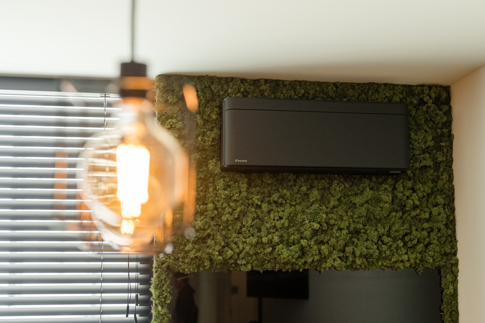 Zwarte Daikin airco geplaatst tegen een wand met groene mosafwerking in een modern, energiezuinig interieur met veel natuurlijk licht.