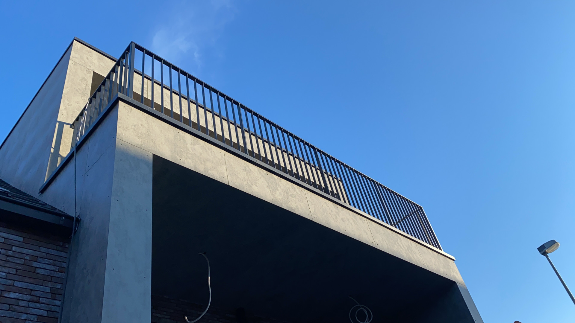 Strakke metalen balustrade op moderne bovenverdieping Gepoederlakte balustrade op maat op een betonnen terrasstructuur, geplaatst door Laswerken Bellon in Sint-Niklaas, onder een heldere blauwe lucht.