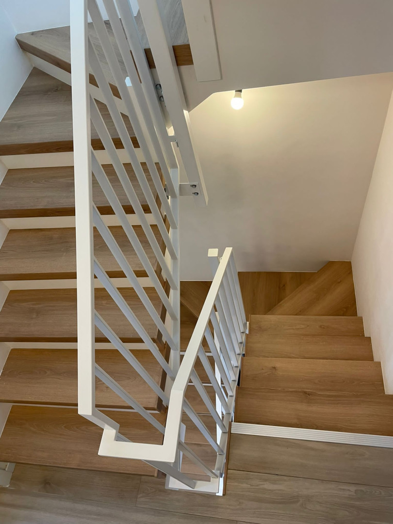 Witte stalen trapleuning met moderne lijnen in interieurwoning Op maat gemaakte witte stalen trapleuning met strakke lijnen langs een houten trap in een moderne woning, vervaardigd door Laswerken Bellon in Sint-Niklaas.