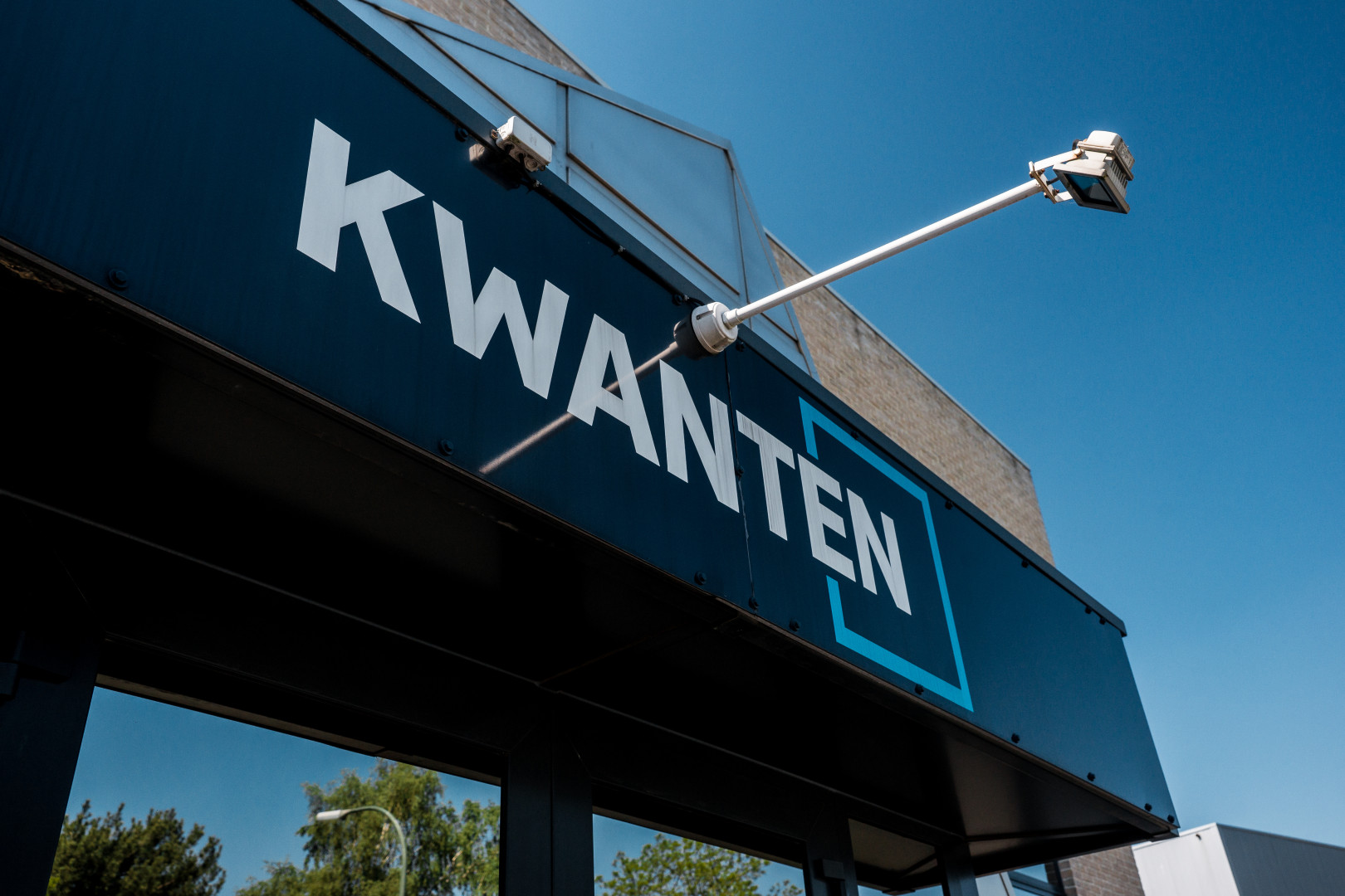 Voorgevel van Tegelhandel Kwanten in Pelt Buitenaanzicht van de ingang van Tegelhandel Kwanten in Pelt, met opvallend blauw uithangbord en moderne gevel tegen een heldere hemel.