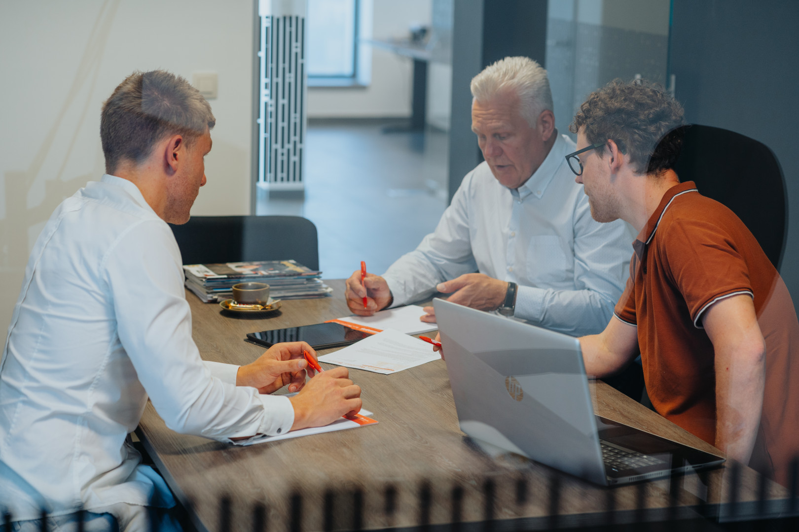 Drie mannen in overleg aan een vergadertafel, bespreken documenten en voertuigregistratie tijdens een adviesgesprek bij AWB.