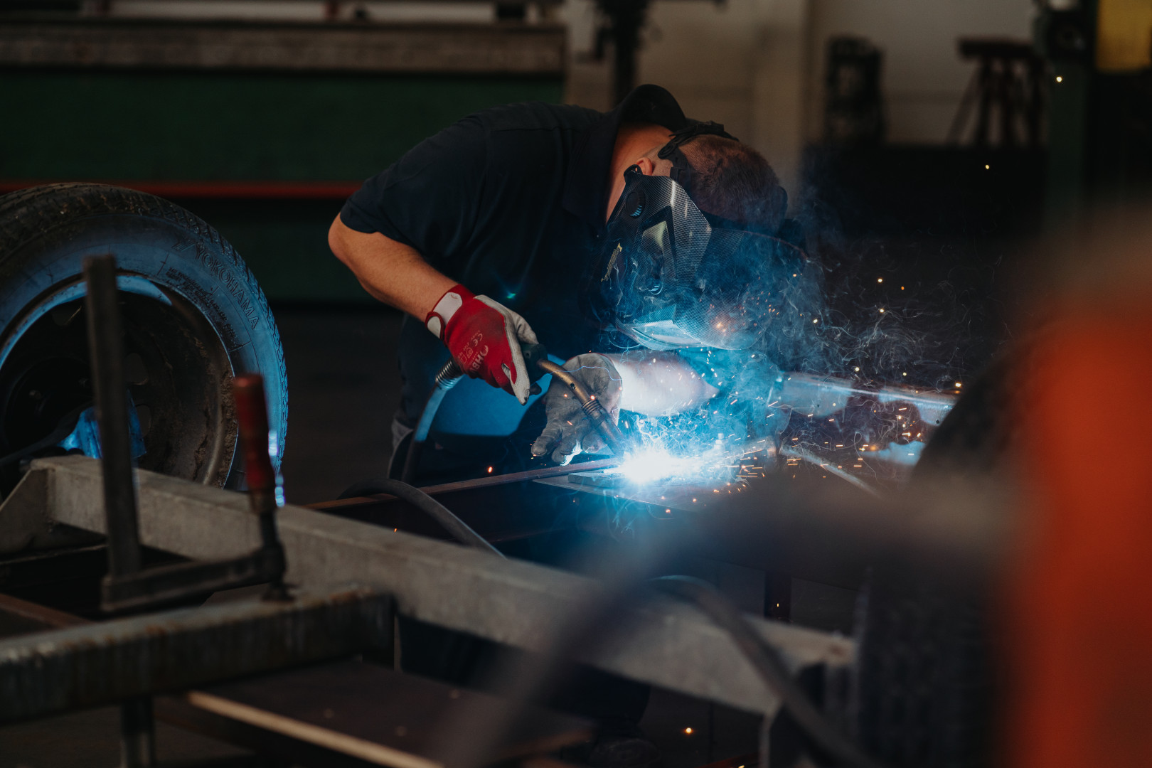 Laswerken aan chassis tijdens ombouw lichte vracht Monteur voert laswerk uit aan het onderstel van een voertuig tijdens de ombouw naar lichte vracht, met beschermende helm en handschoenen.