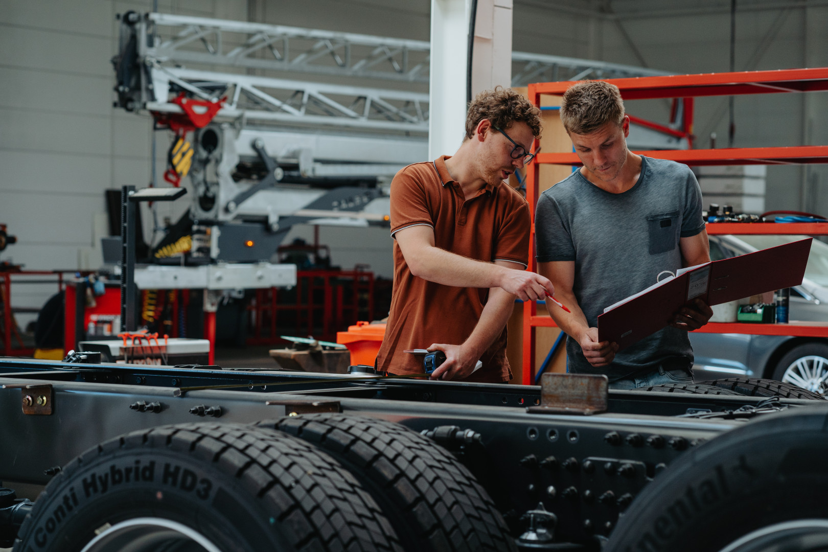 Technische controle en voorbereiding bij ombouw lichte vracht Twee mannen bespreken technische specificaties aan een chassis in de werkplaats van AWB tijdens de voorbereiding van een lichte vracht ombouw.