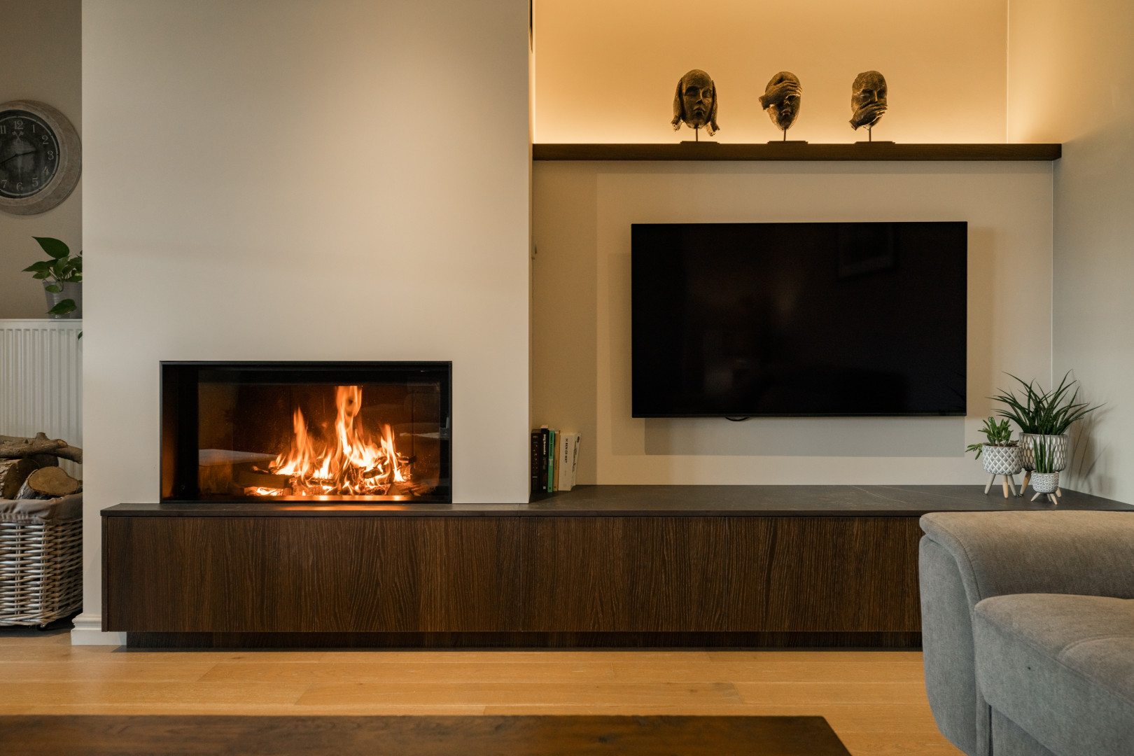 Houthaard ge&iuml;ntegreerd in maatwerkmeubel met donkere houtafwerking en wandgemonteerde tv, afgewerkt met sfeerverlichting en decoratieve accenten.