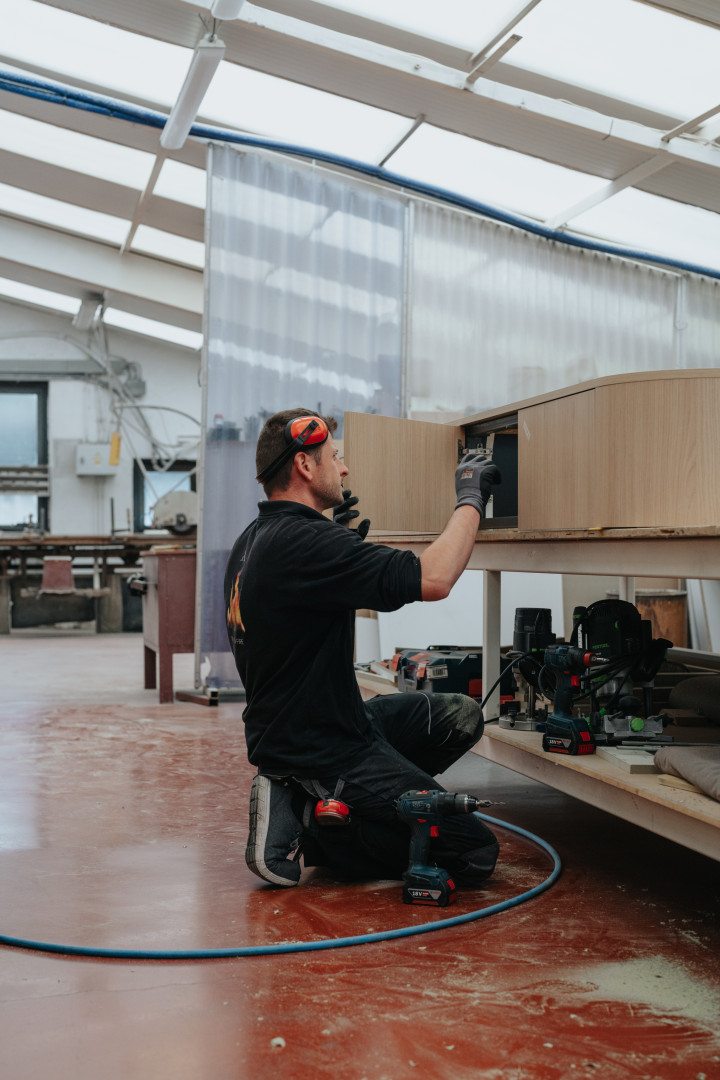 Vakkundige afwerking van maatmeubel in het atelier van Schouwen André Maatschrijnwerker aan het werk in het atelier van Schouwen André, bezig met het fijn afstellen van een houten maatkast met professioneel gereedschap.