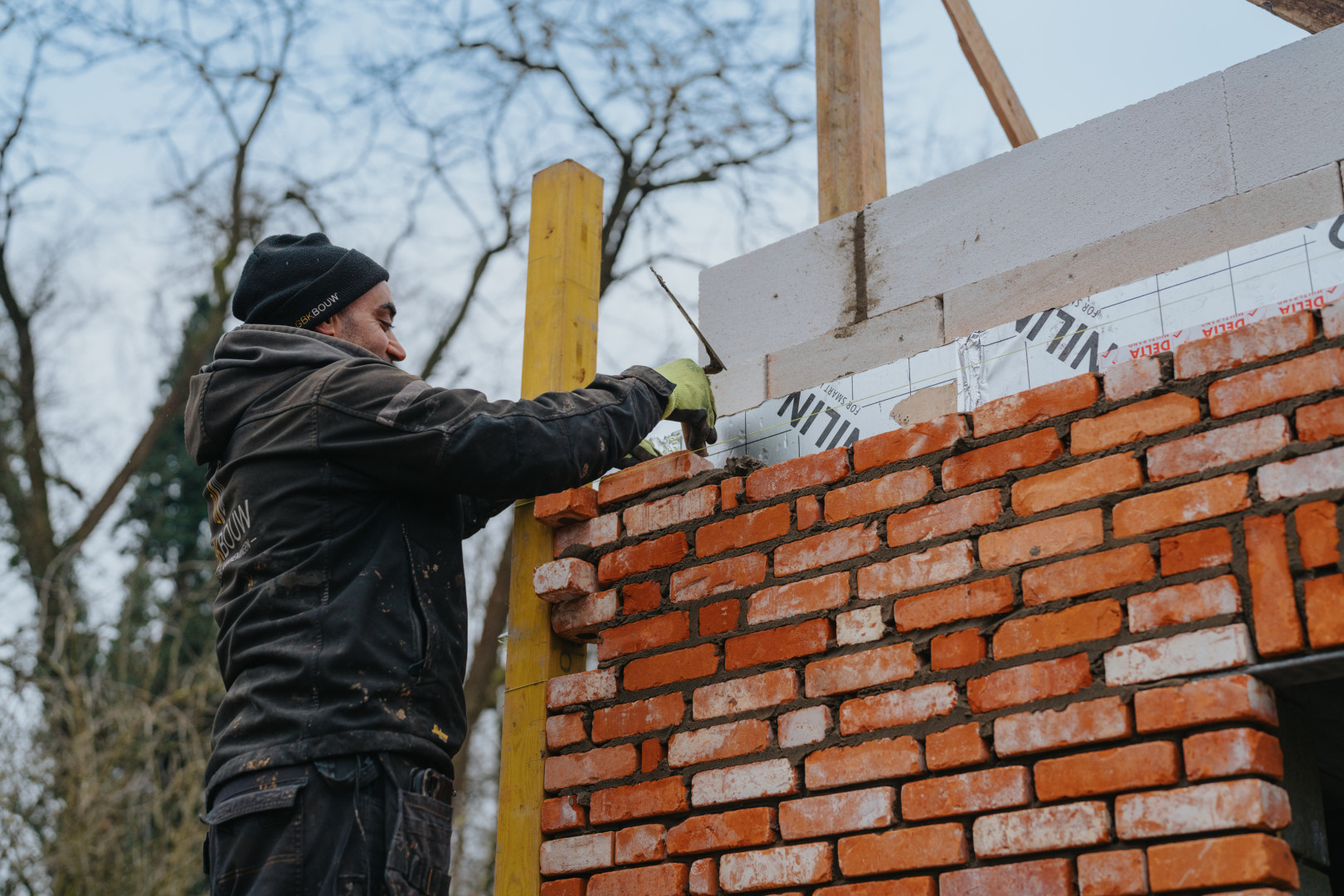 Metselwerken in uitvoering bij nieuwbouwproject van GBK Bouw Metselaar van GBK Bouw aan het werk tijdens de ruwbouwfase van een nieuwbouwwoning, met zicht op rode gevelstenen en isolatiepanelen.