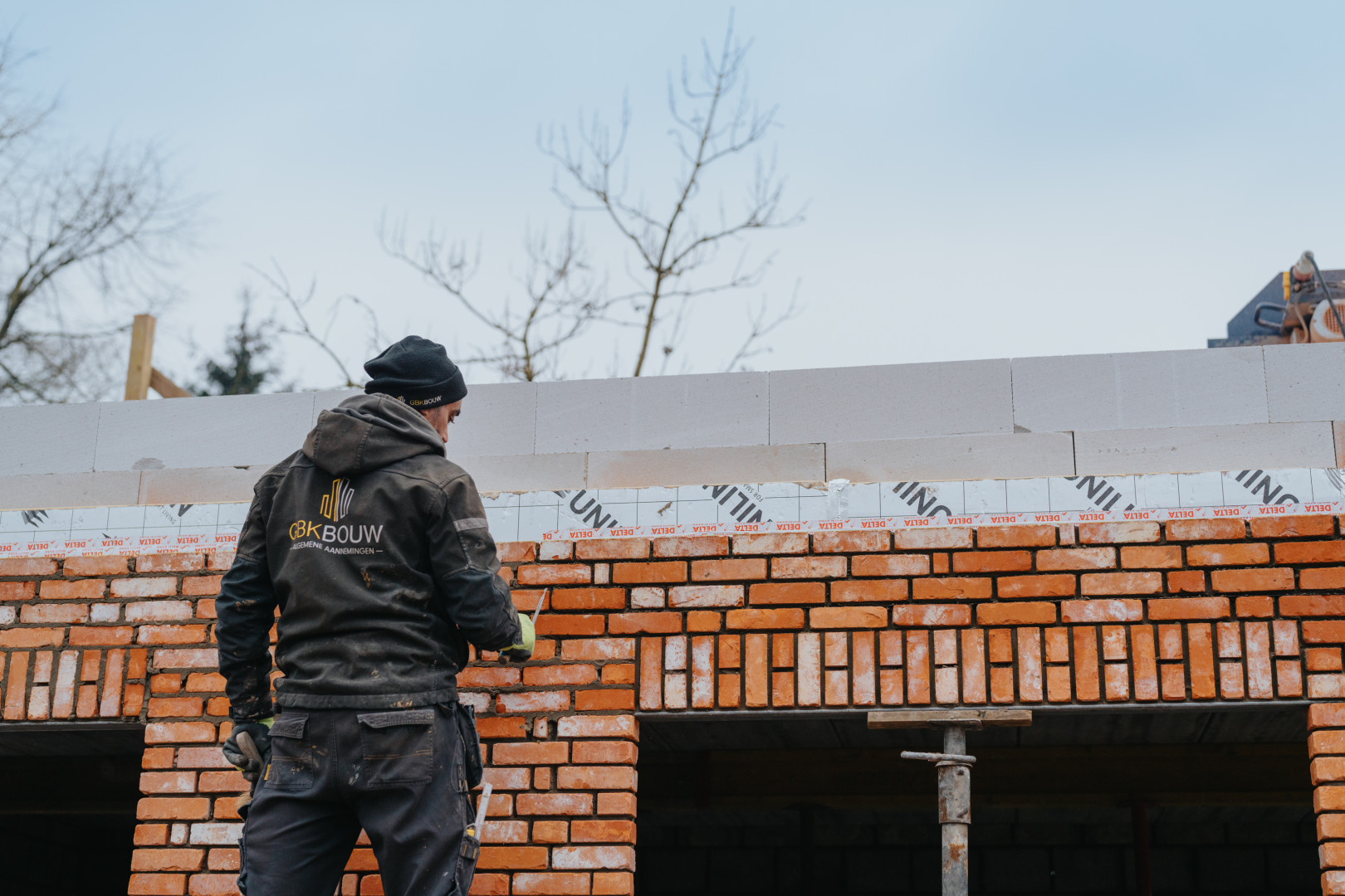 Gevelmetselwerken in uitvoering door GBK Bouw Metselaar van GBK Bouw aan het werk tijdens gevelmetselwerken aan een nieuwbouwwoning, met rode gevelstenen en isolatiepanelen op de achtergrond.