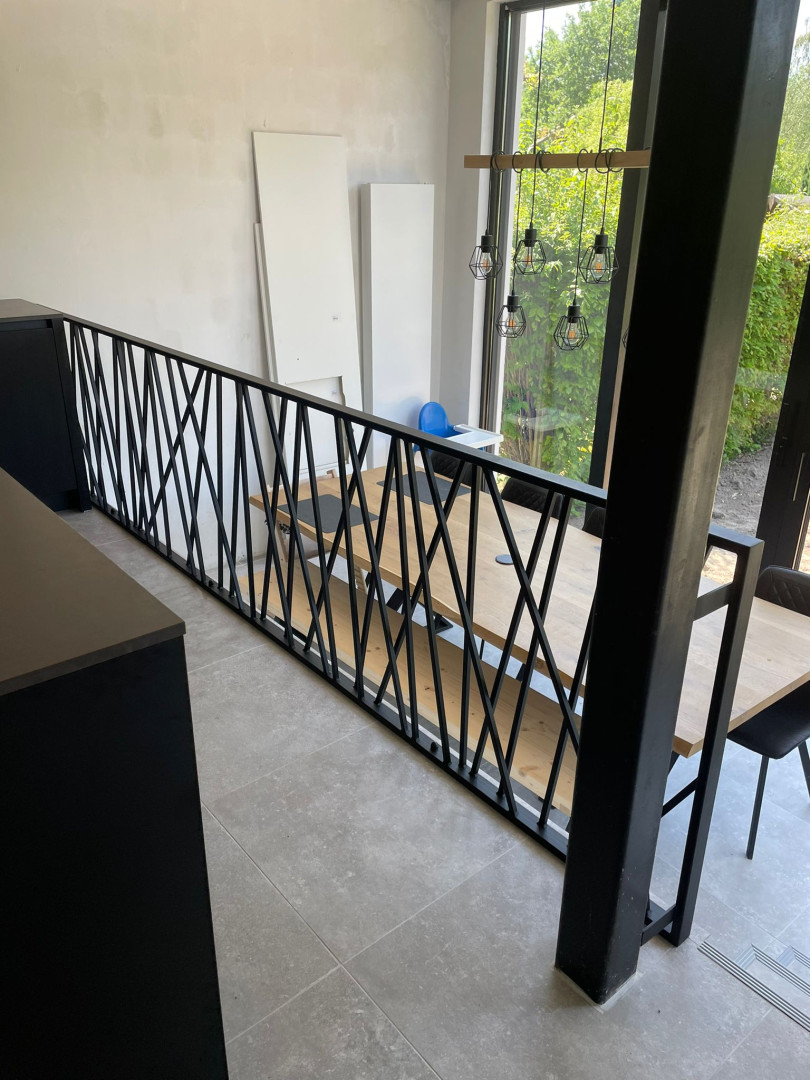 Stijlvolle zwarte balustrade met speels lijnenspel, geplaatst op een mezzanine in een moderne woning in Sint-Niklaas, op maat gelast door Laswerken Bellon.