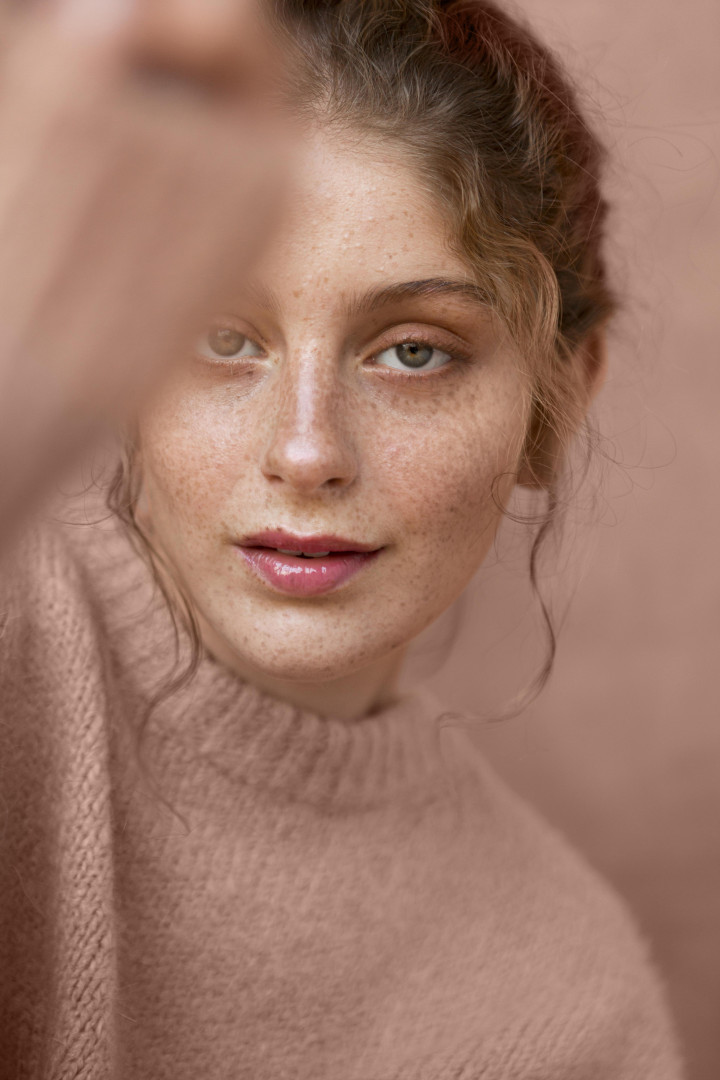 Stralende huid na dermaplaning behandeling Jonge vrouw met een egale, stralende huid en natuurlijke make-up poseert in een roze trui voor een ton-sur-ton achtergrond, symbool voor huidverbetering na dermaplaning.