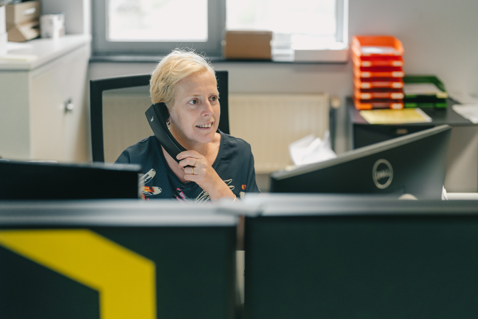Vrouwelijke medewerker met kort blond haar aan de telefoon achter bureau