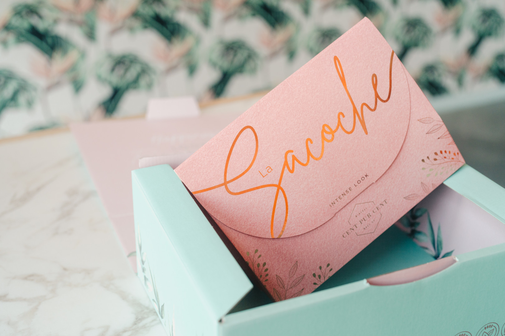 Pastelkleurige roze en blauwe kartonnen productverpakking met koperkleurige letters